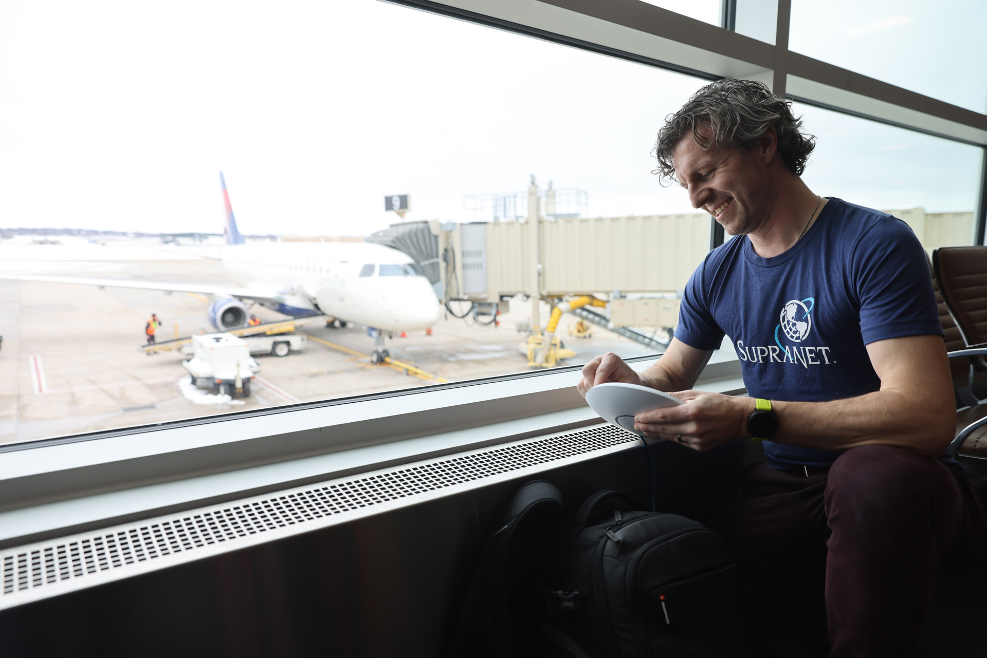 Man in front of window at airport. Airplane and jetway outside. Access point in hand