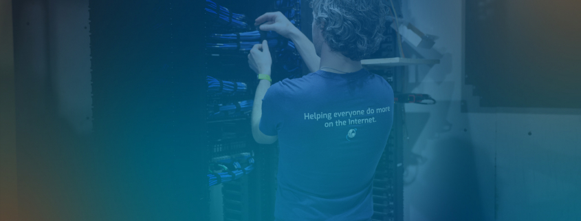 Person with back to camera working on wires in data center. SupraNet shirt that says "Helping Everyone do more on the Internet."